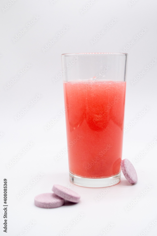 In a glass with pink red water, a soluble, instant or dissolve pink tablet bubbles. Nearby are similar tablets: vitamin C, dietary supplements, painkillers In a glass with pink red water, a soluble, instant or dissolve pink tablet bubbles. Nearby are similar tablets: vitamin C, dietary supplements, painkillers
