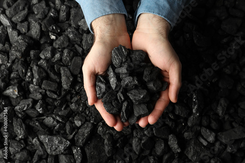 Man holding coal in hands over pile, top view