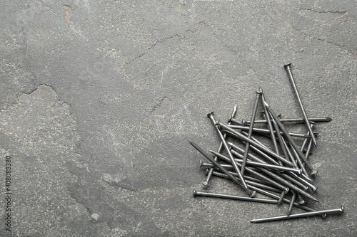 Pile of metal nails on grey stone background, flat lay. Space for text