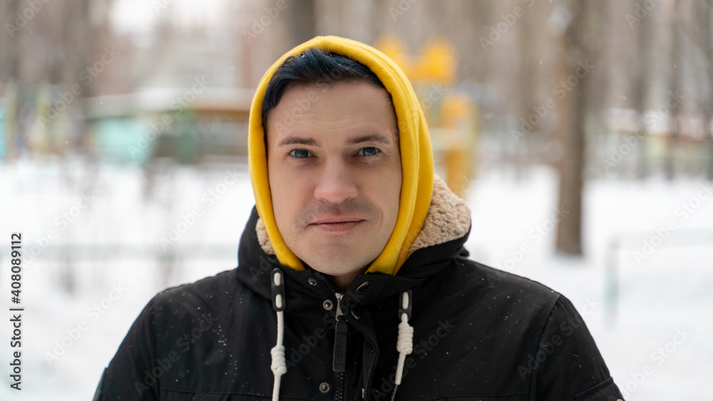 Portrait of young man in yellow hood on street in winter. Close up of adult male posing on walk in winter season. Portrait of young man in yellow hood on street in winter. Close up of adult male posing on walk in winter season.