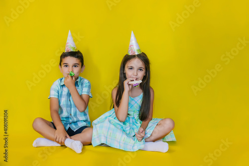A little girl and a boy are sitting on the floor in their holiday hats.The concept of a holiday and a birthday.