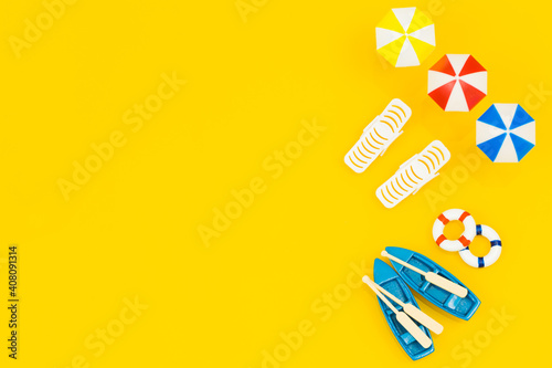 Miniature beach equipment, umbrellas, boats, sun loungers. blank yellow background with space for text, concept, Sunny beach vacation.