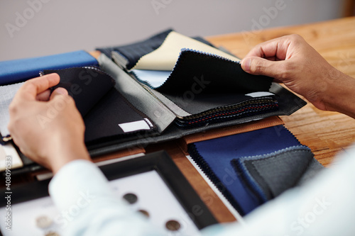 Hands of tailor touching two types of black wool fabric to choose for making bespoke suit photo