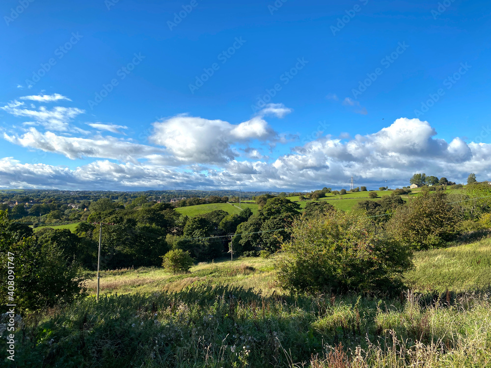 Rural landscape, looking over fields, trees, and farms, under a blue sky in, Clifton, Brighouse, UK