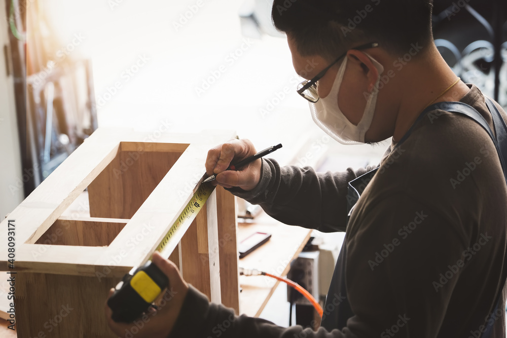 A carpenter measures the planks to assemble the parts, and build a wooden table for the customer A carpenter measures the planks to assemble the parts, and build a wooden table for the customer