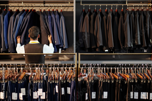 Shop assistant checking jackets on hanger in men clothing store, view from the back