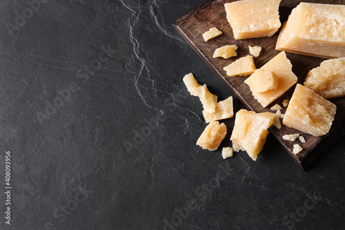 Pieces of delicious parmesan cheese on black table, top view. Space for text