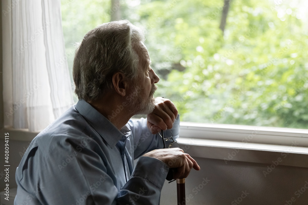 Close up thoughtful mature man holding cane and glasses, looking out window, lost in thoughts, remembering past, sitting alone, pensive lonely elderly male using walking stick during rehabilitation Close up thoughtful mature man holding cane and glasses, looking out window, lost in thoughts, remembering past, sitting alone, pensive lonely elderly male using walking stick during rehabilitation