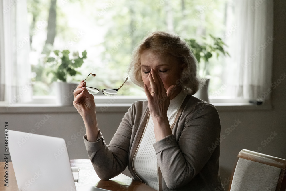 Exhausted stressed mature woman taking off glasses, touching massaging nose  bridge, tired aged female suffering from eye strain after long laptop use,  dry eyes syndrome, sitting at table at home Photos