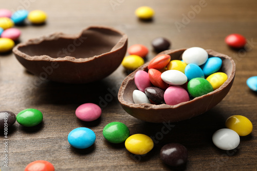 Broken chocolate egg and colorful candies on wooden table, closeup