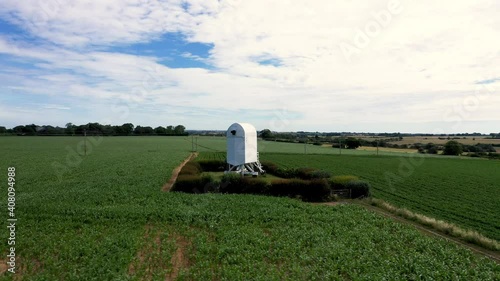 Drone shot circling an isolated windmill without sails surrounded by farmland on a windy day.