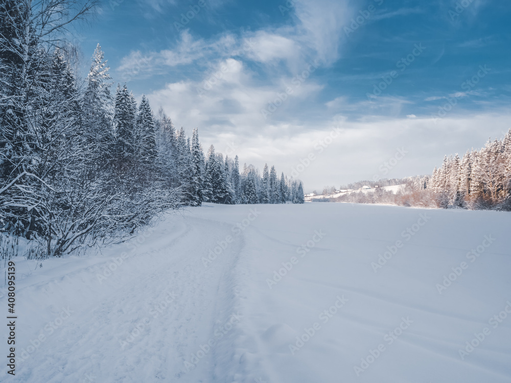 Snowy road and conifer forest on a frosty sunny evening. Winter country road with fir forest in the rays of cold winter Sun. Snowy road and conifer forest on a frosty sunny evening. Winter country road with fir forest in the rays of cold winter Sun.