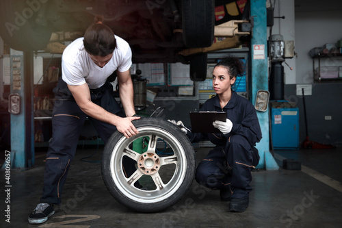 Two mechanic checking wheels at garage, car service technician man and woman checking and repairing the customer car at automobile service center, vehicle repair service shop concept