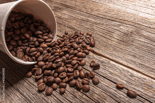 Paper cup with coffee beans on a wooden table.