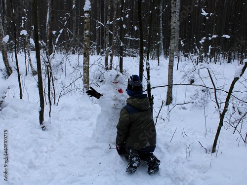 a boy makes a big snowman in the forest