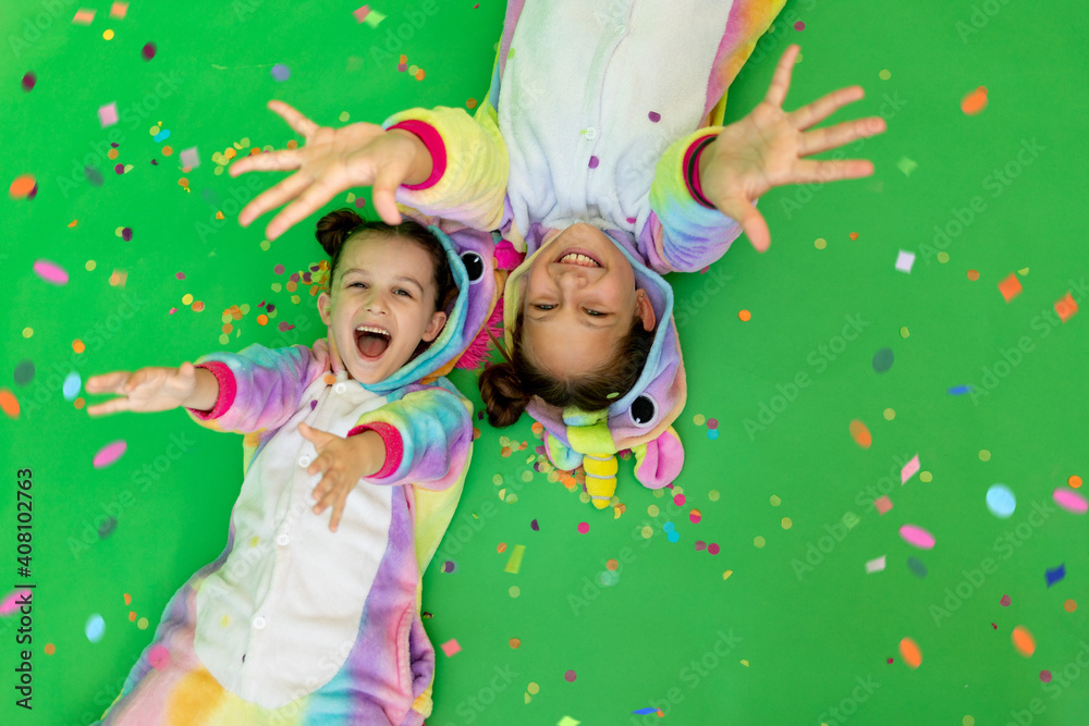 little girls in bright costumes lie on a green isolated background with a streamer in bright unicorn costumes. The concept of a holiday, Birthday and sales