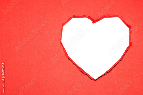 Heart-shaped white hole torn through the red paper. Valentine's Day idea
