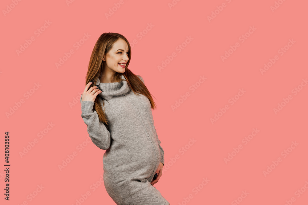 Pregnant woman. Expectation of the child. Maternity leave. Pregnancy of a happy beautiful girl in a gray sweater on a pink background Pregnant woman. Expectation of the child. Maternity leave. Pregnancy of a happy beautiful girl in a gray sweater on a pink background