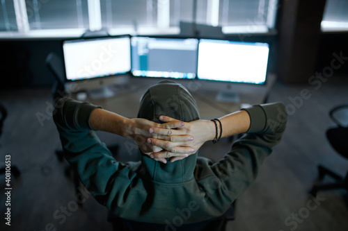 Male hacker in hood sitting at screens, back view