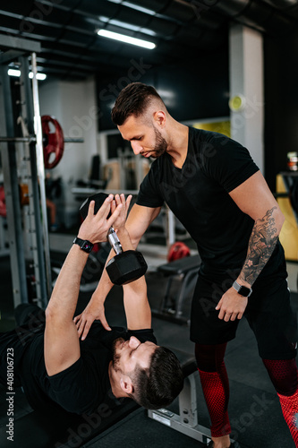 Personal trainer helping, assisting client in the gym and doing chest dumbbells workout. Healthy lifestyle fitness session with personal trainer.
