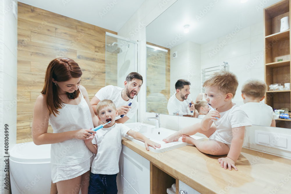 Fototapeta premium Young happy family man, woman and two small children, two boys in a backpack brushing teeth together in the bathroom