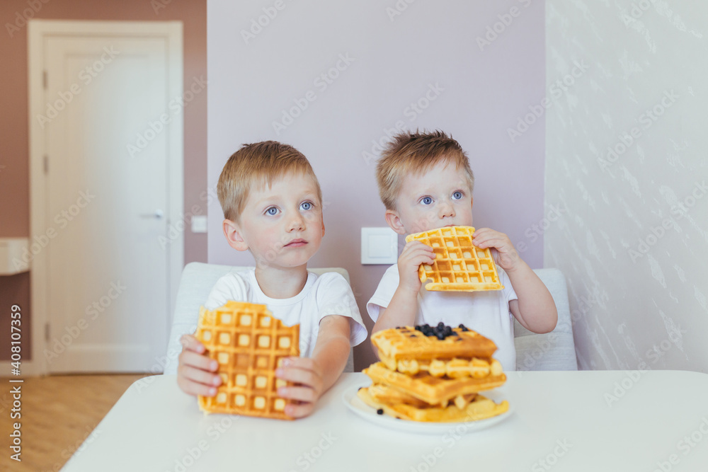 Two little boys in the kitchen holding waffles and having breakfast, brothers Two little boys in the kitchen holding waffles and having breakfast, brothers