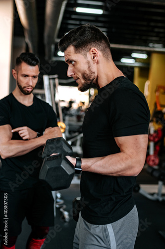 Portrait of male personal trainer helping out and assisting clients in the gym. Fitness details of healthy life, dumbbell training