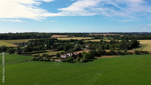 Drone shot circling around farmhouses and trees surrounded by countryside on a sunny day. 4k