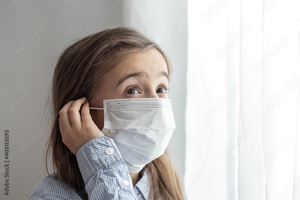 Little girl in a protective medical mask stands near the window close up. Little girl in a protective medical mask stands near the window close up.