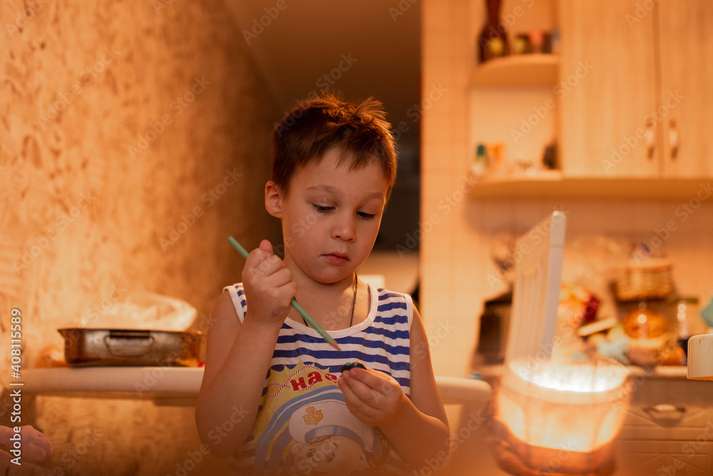 a boy at home in the kitchen in a striped T-shirt stands and sharpens a green pencil with a sharpener a boy at home in the kitchen in a striped T-shirt stands and sharpens a green pencil with a sharpener