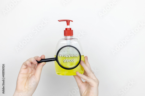 A woman examines the harmful ingredients of the liquid soap a magnifying glass. Harmful composition of ingredients. Means with Propylene glycol photo