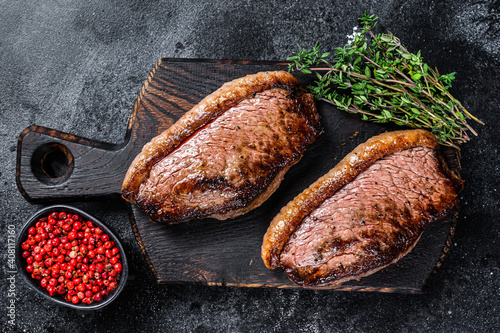 BBQ Grilled top sirloin cap or picanha steak on a wooden cutting board. Black background. Top view photo