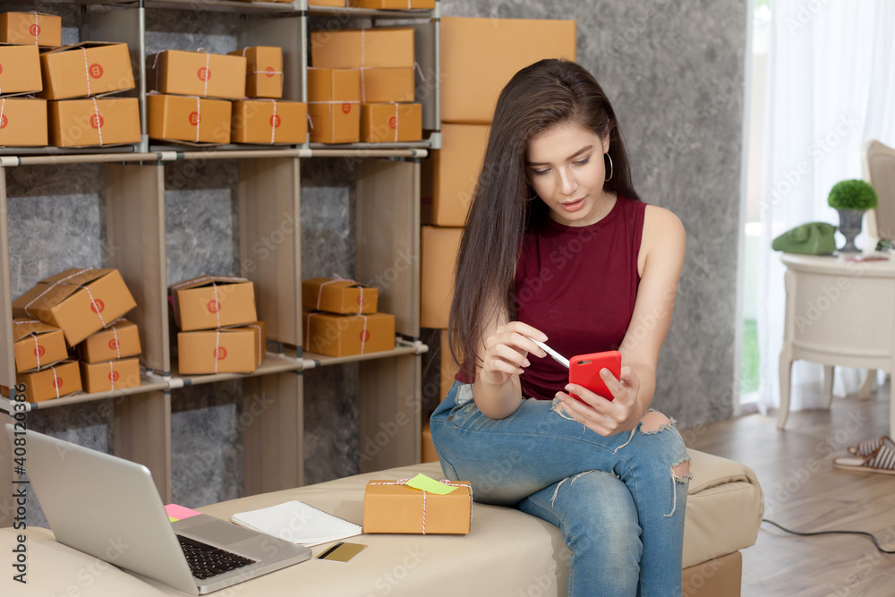 Online business owner. Asian woman in a casual workday packing products taking order customers using smartphone and laptop at home. Online business owner. Asian woman in a casual workday packing products taking order customers using smartphone and laptop at home.