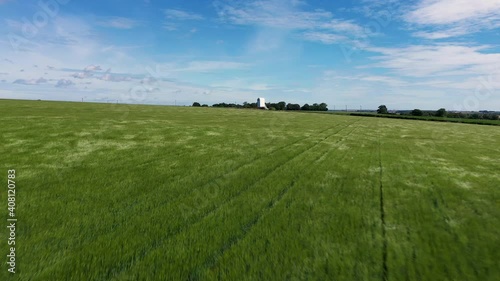 Low angle drone shot flying over blowing grass approaching a windmill without sails.