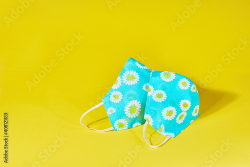 Handmade blue cotton masks with chamomile ornament on a yellow background. Homemade masks with smile. DIY face mask for safety at pandemic or quarantine. Spring concept