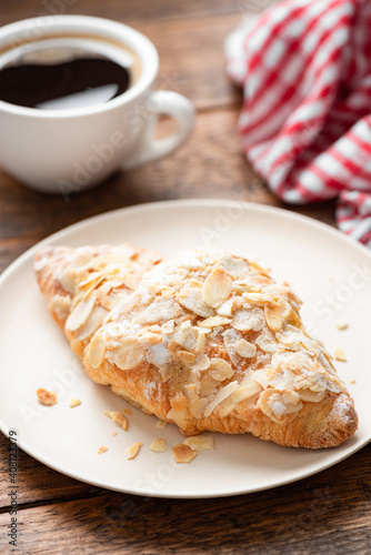 Almond croissant and cup of coffee on a wooden table. Breakfast in cafe