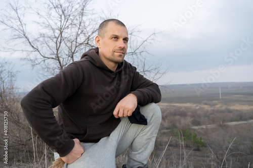 A man sits on the edge of a cliff over which a large valley is visible