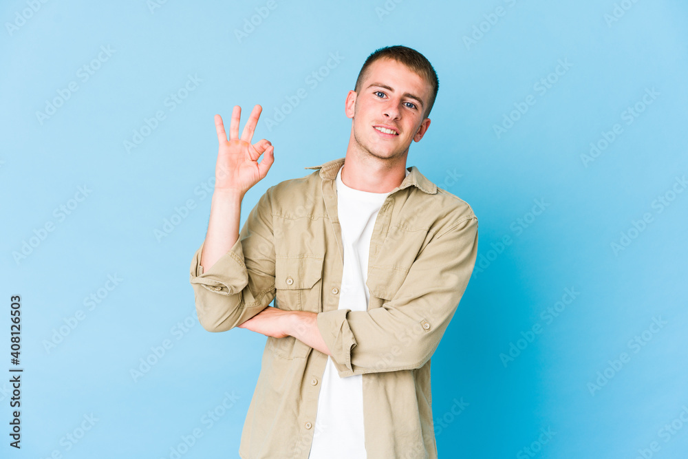 Young caucasian handsome man winks an eye and holds an okay gesture with hand. Young caucasian handsome man winks an eye and holds an okay gesture with hand.