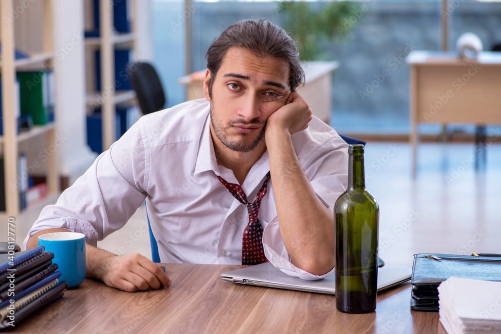 Young male alcohol addicted employee working in the office Young male alcohol addicted employee working in the office