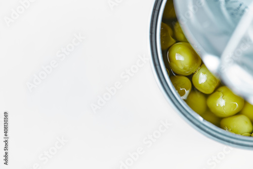 Opened tin with boiled green peas on a white background