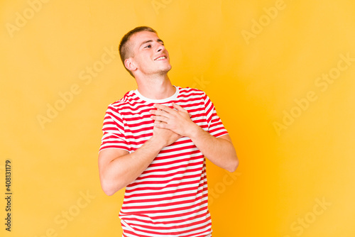 Young caucasian handsome man laughing keeping hands on heart, concept of happiness.