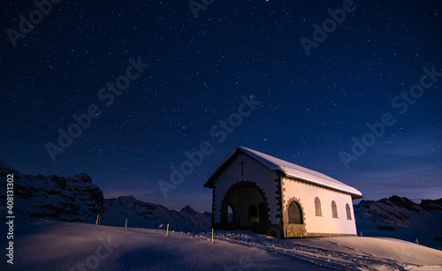 amazing winter night in the Swiss alps. bright stars, mountains, snow and a church in front in Melchsee-Frutt, Switzerland