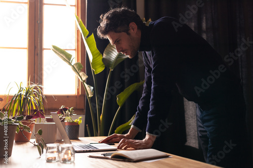 Young man working on laptop standing up in a cosy environment. Creative business man. Hipster working remotely while confined.