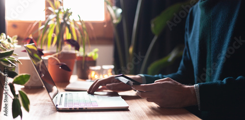Closeup on male hands working on smartphone and laptop. Young man connecting to internet in a cosy environment.