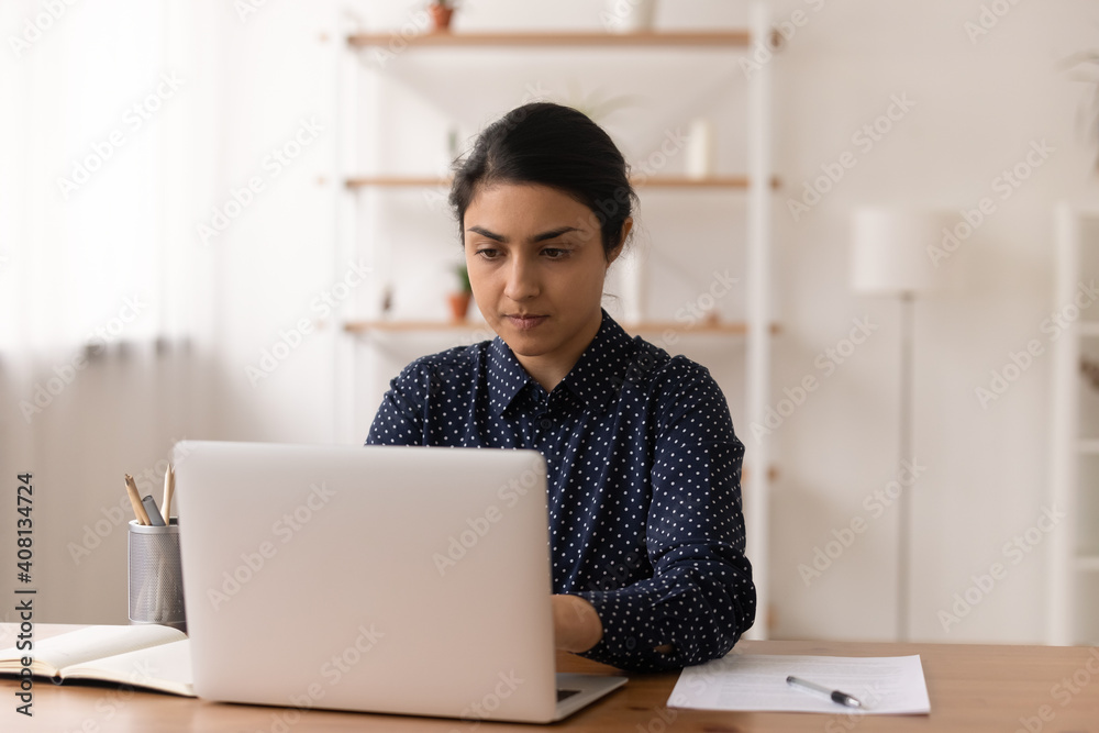 Busy indian lady freelancer engaged at computer work typing writing electronic document text on pc keyboard. Confident young woman remote worker student focused on laptop screen doing project research Busy indian lady freelancer engaged at computer work typing writing electronic document text on pc keyboard. Confident young woman remote worker student focused on laptop screen doing project research