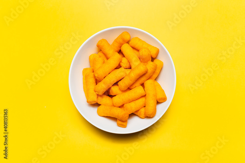 Top view of white bowl with corn puffs on yellow background.