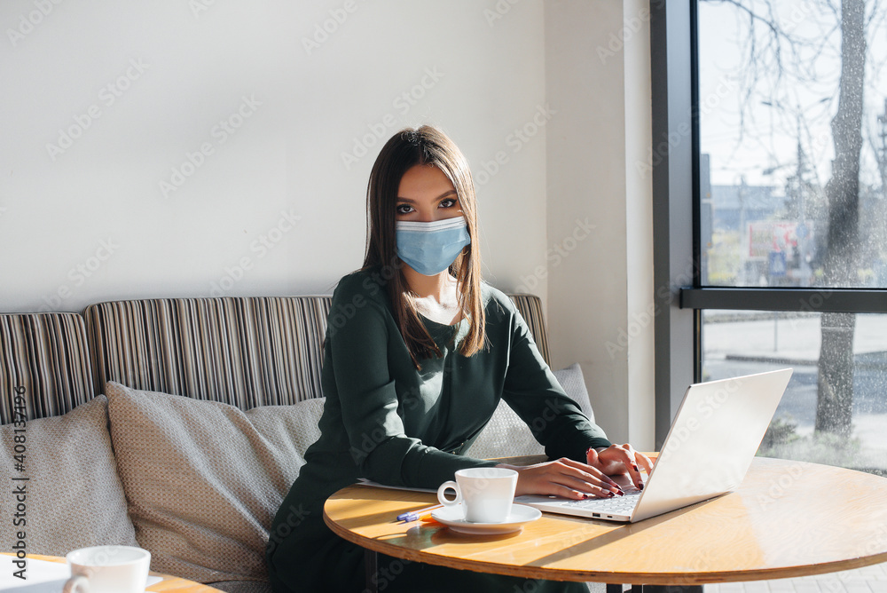 A young girl is sitting in a cafe wearing a mask and working at a computer. A young girl is sitting in a cafe wearing a mask and working at a computer.
