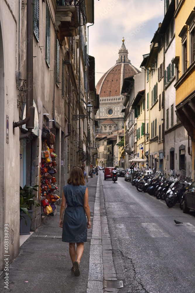 Frau geht durch Gasse von Florenz vor Kuppel der Kathedrale Santa Maria del Fiore zwischen Häusern