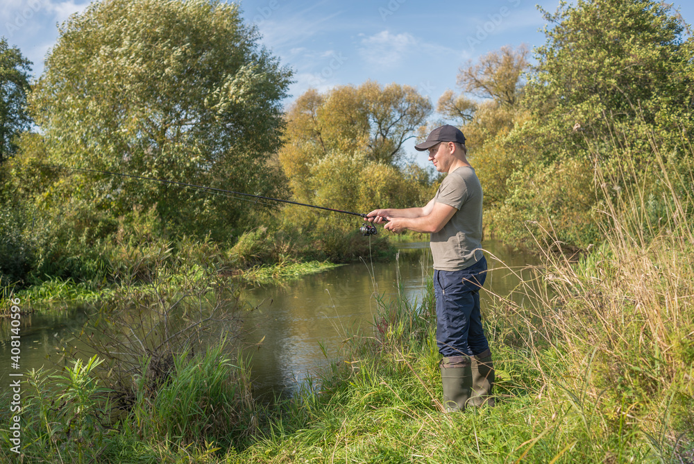 Fisherman holding a fishing rod by the river. Summer sunny day