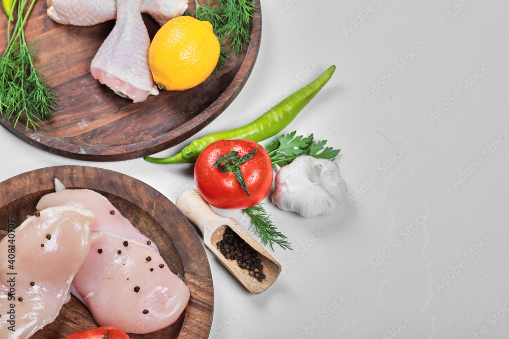 Two wooden bowls of raw chicken legs and fillet with fresh vegetables on white background Two wooden bowls of raw chicken legs and fillet with fresh vegetables on white background